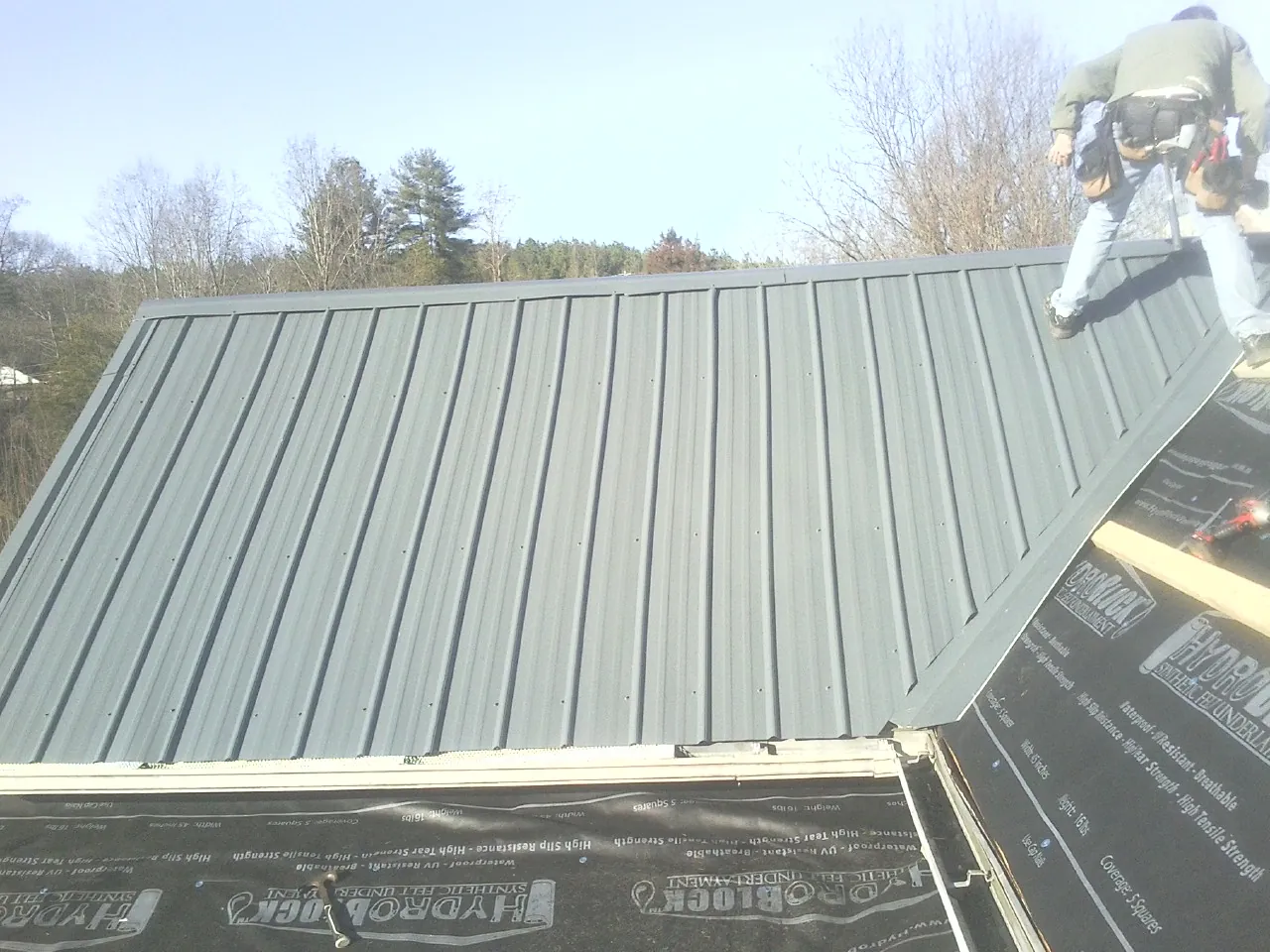 Crew installing dark green standing seam panels over synthetic underlayment in Canyon Dam