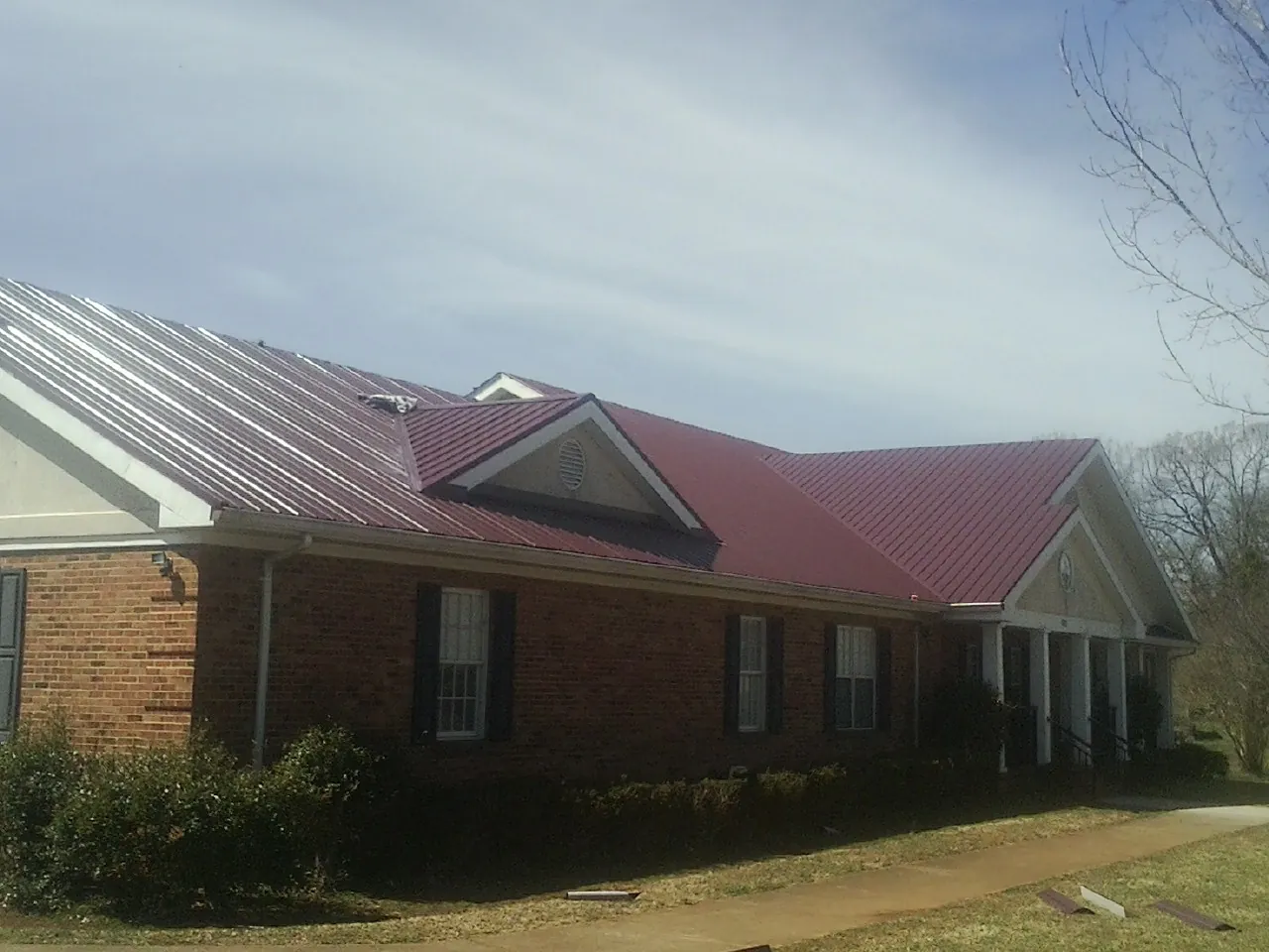 Red metal roof with gabled entries on a long brick building, from a Hail Damage Roof Repair job in Canyon Dam