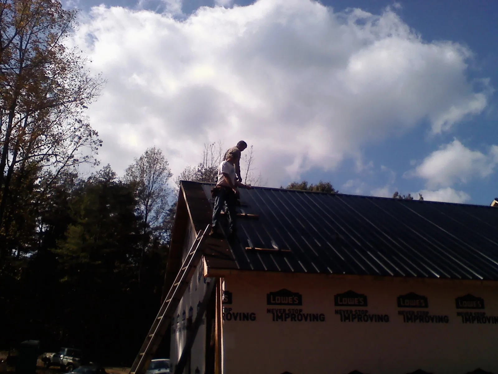 Roofer fastening dark metal panels high against a cloudy sky, from a Roof Inspection job in Canyon Dam