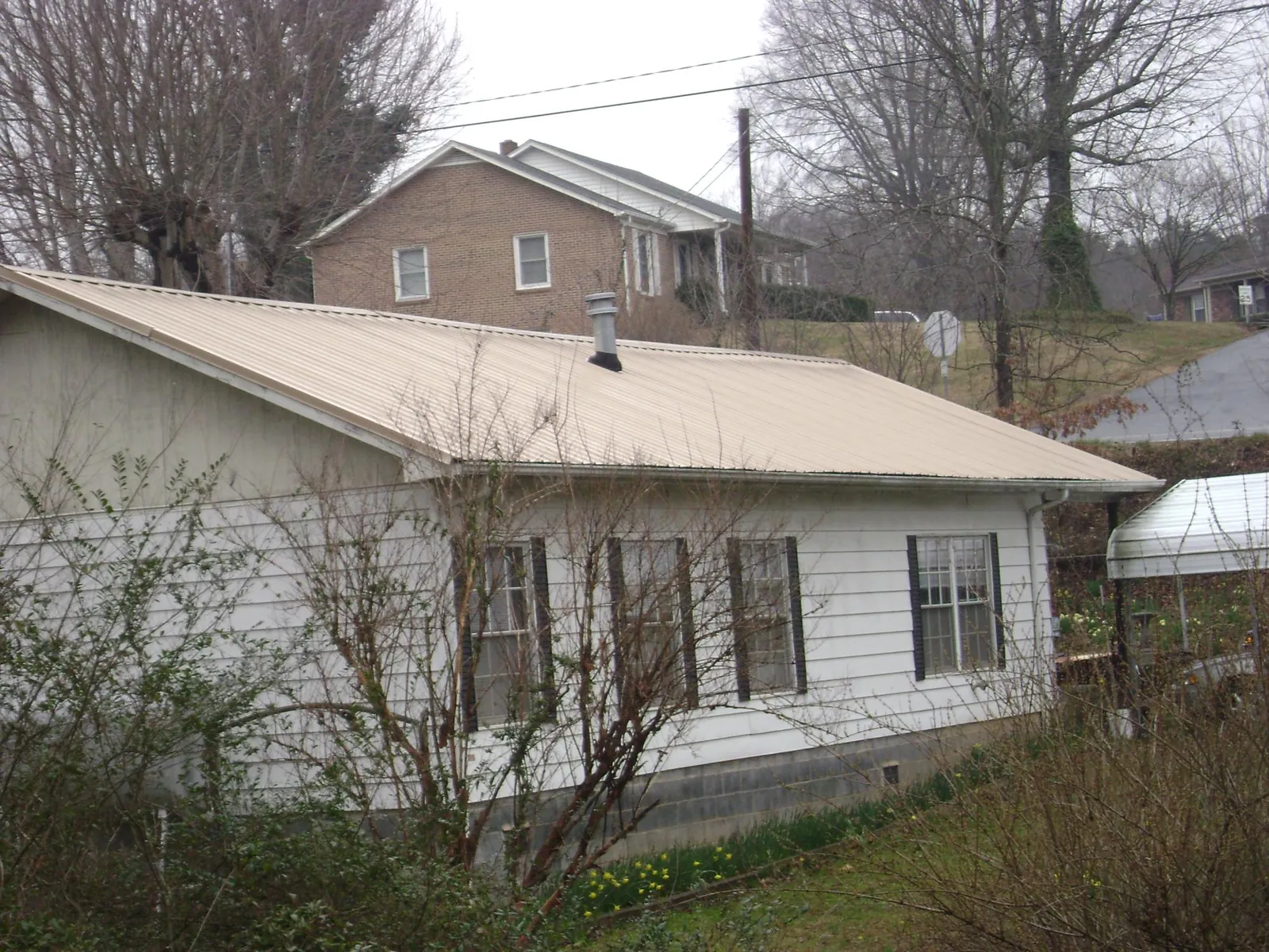 Tan metal roof on a white sided house set into a hillside — Commercial Roofing by Roofing Brothers in Canyon Dam